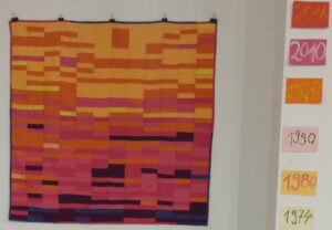 Photo of quilt hanging on the wall of an exhibition space