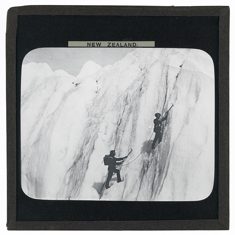 'Step Cutting on Ice Face, Tasman Glacier, New Zealand'. Photograph of two men step cutting on the ice face of the Tasman Glacier, New Zealand in the late 19th or early 20th century.