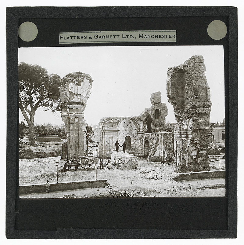 'Ruins'. Photograph of ruins of a church or other building with two people dressed as British policemen hold hands as they stand on a platform and two men stand to the side with a horse and cart in the early 20th century.