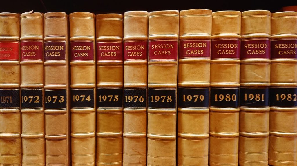 A row of leather bound books fills the frame from left to right. The title 'Session Cases' and the year are embossed on the spines. The leather is blonde and each spine has a red and black square. 