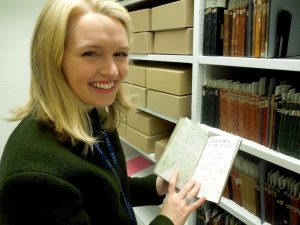 Elise Ramsay, Project Archivist, holding an open scientific notebook and smiling