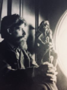 Black and white photograph of Sir Patrick Geddes sat in a window recess with a sculpture (unidentified) to his right.