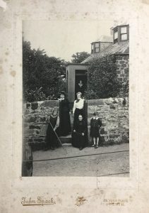 Black and white photograph taken by John Spark of Perth showingAnna Geddes, Miss Scott, Janet Cuthbertson, Norah and Alasdair Geddes at the garden gate of Mount Tabor cottage, Perth, c.1899