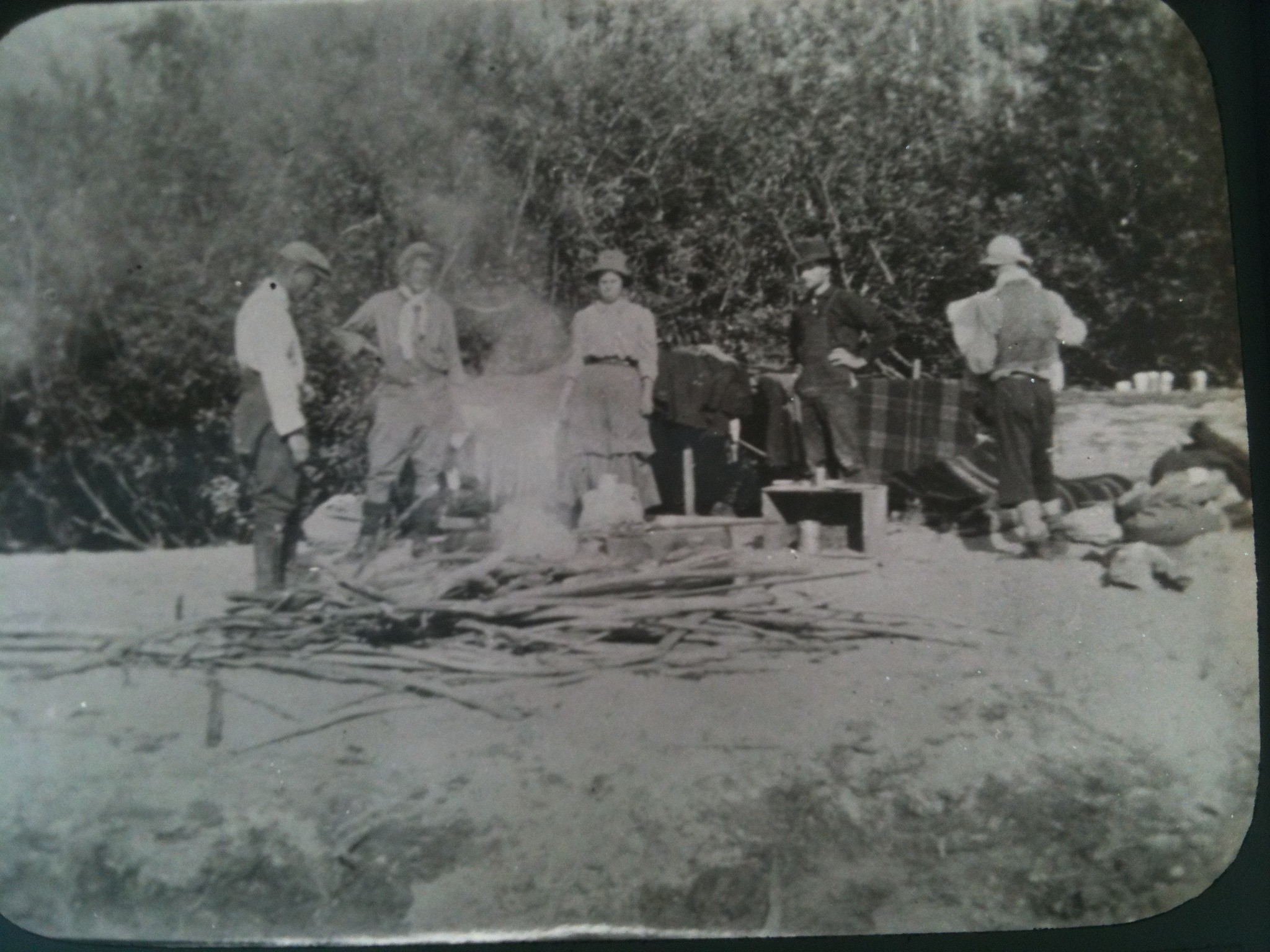 Photograph of a group of men and a woman standing around a camp fire in camp in British Columbia, Canada in the early 20th century. One of the men may be Professor Robert Wallace, another man may be Alex Easton and the woman may be Isabel Easton. 