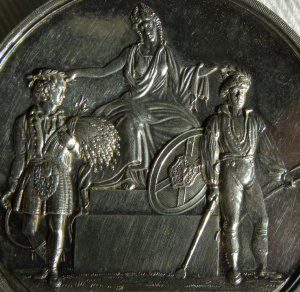Detail, obverse, silver medal, Highland and Agricultural Society of Scotland, decorated with raised seated classical figure with Scottish armorial shield honouring figures representing agriculture and industry
