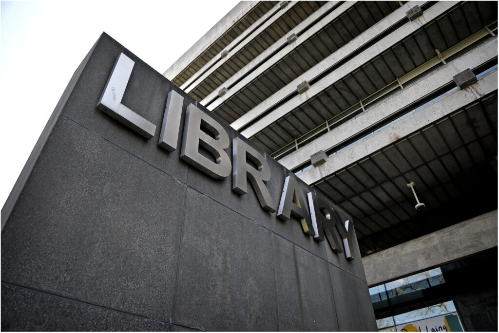 Metal sign outside the Main Library, taken from a low angle at the bottom of the stairs. The word Library is spelled out in silver coloured letters mounted on a large stone wall.