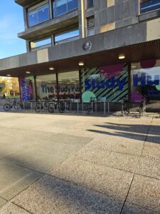 Exterior of a modern building with large windows displaying colorful "Study Hub" signage; several bicycles are parked in racks outside.