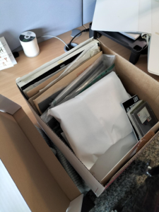 Colour photograph of a cardboard box with the lid off. Inside are folders, papers and photographs. 