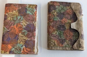Image of a paper bound volume with a brocade paper wrapper. The paper paper has a gold background and swirling flower pattern with many different colours. 
