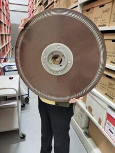 A member of staff holds a large brown disk up for the camera. The disk obscures their face down to the hips.