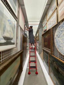 Woman at the top of a red ladder placing a framed artwork on picture racking