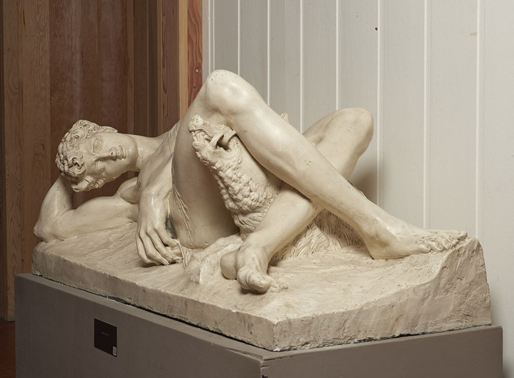 Plaster cast sculpture of Clement Pappi's 'Dying Adonis' sculpture. The sculpture shows a reclining nude male figure with an agonized expression, who's thigh is being gored by a small boar. 