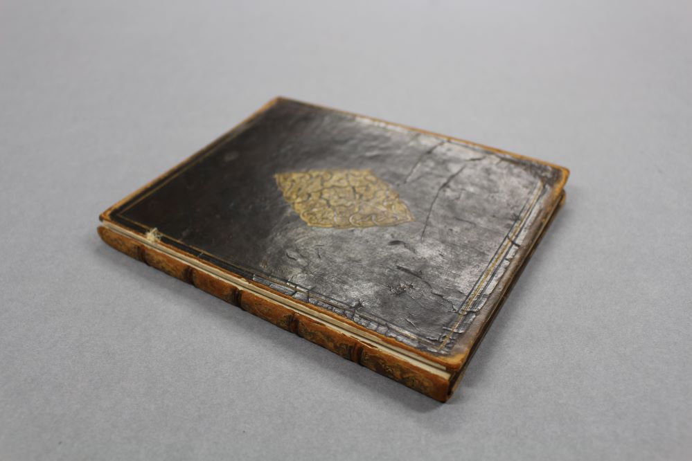 A brown leather book with gold decoration. The front cover is detached.