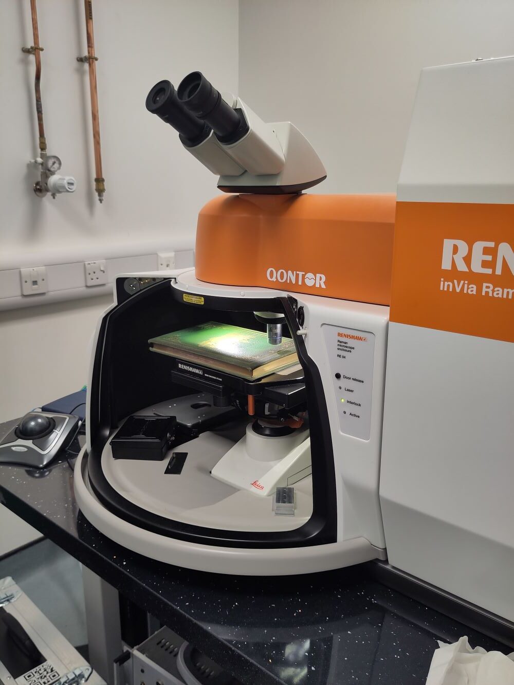 A green book lying under a microscope inside an orange and white plastic chamber