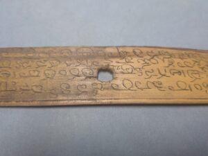 A palm leaf inscribed with text. Half is covered with surface dirt and the other half has been cleaned. 