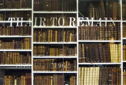 Shelves containing old books from University of Edinburgh Library's Special Collections. Shelves are behind glass which has the phrase 'Thair to Remain' and the dates 1878, 1962 & 1967 stencilled onto the glass.