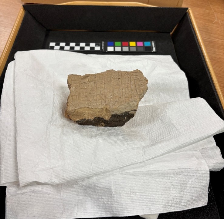 Piece of stone (cuneiform tablet) place on wrapping paper, in a tray with colour guidance strips.