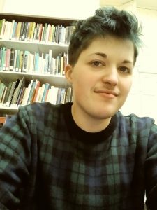 Elliot sits in the library. There are shelves of books behind him