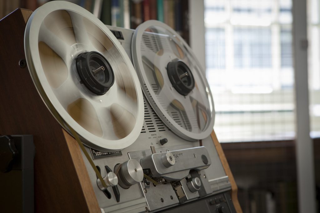 colour photograph of a reel to reel machine in action. The focus over the reels is blurred to show the fast movement