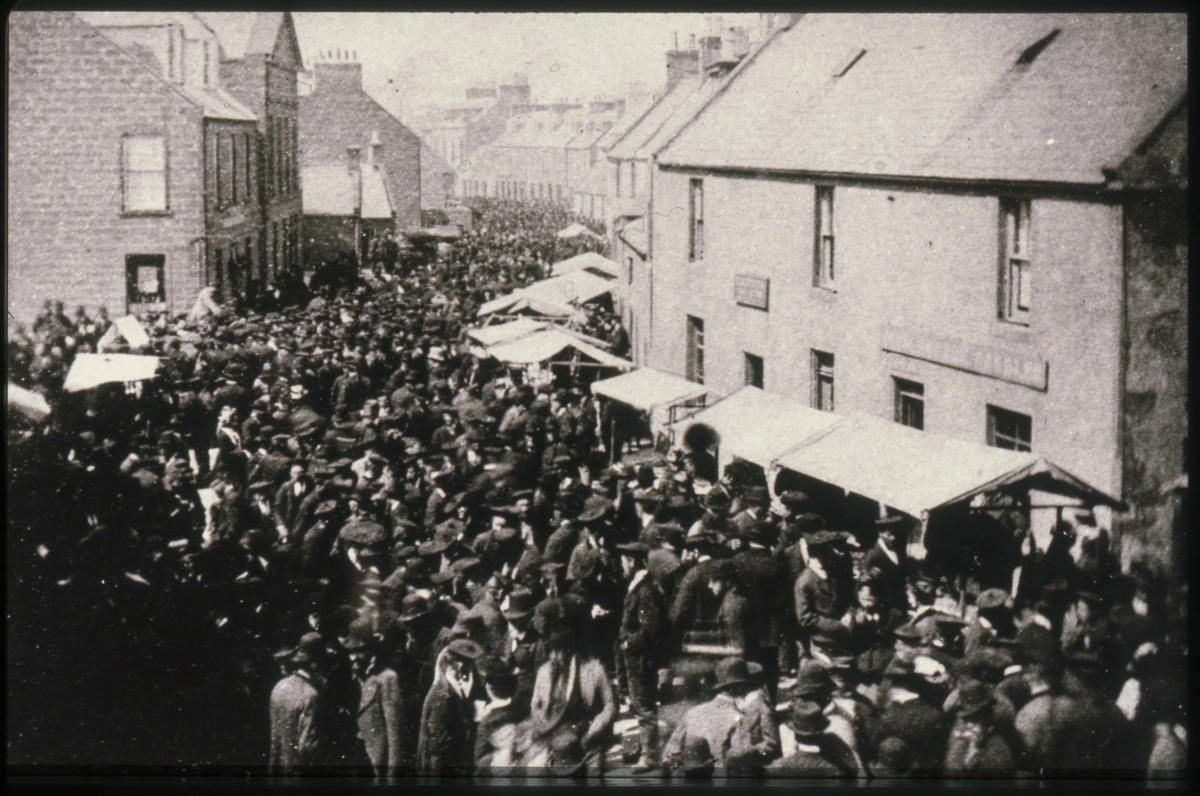 A black and white image of a tightly packed street, with hundreds of people. 